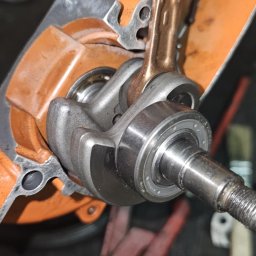 Liwiusz Stoppa - Rozłożony silnik spalinowy z widocznym wałem korbowym, tłokiem i łożyskami. Pomarańczowa obudowa silnika, narzędzia w tle. Precyzyjna naprawa silnika.