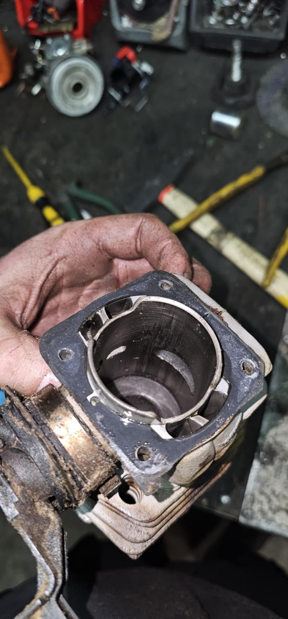 Cylinder silnika spalinowego w dłoni mechanika, widoczne ślady zużycia i nagaru. Detal z warsztatu, narzędzia w tle.