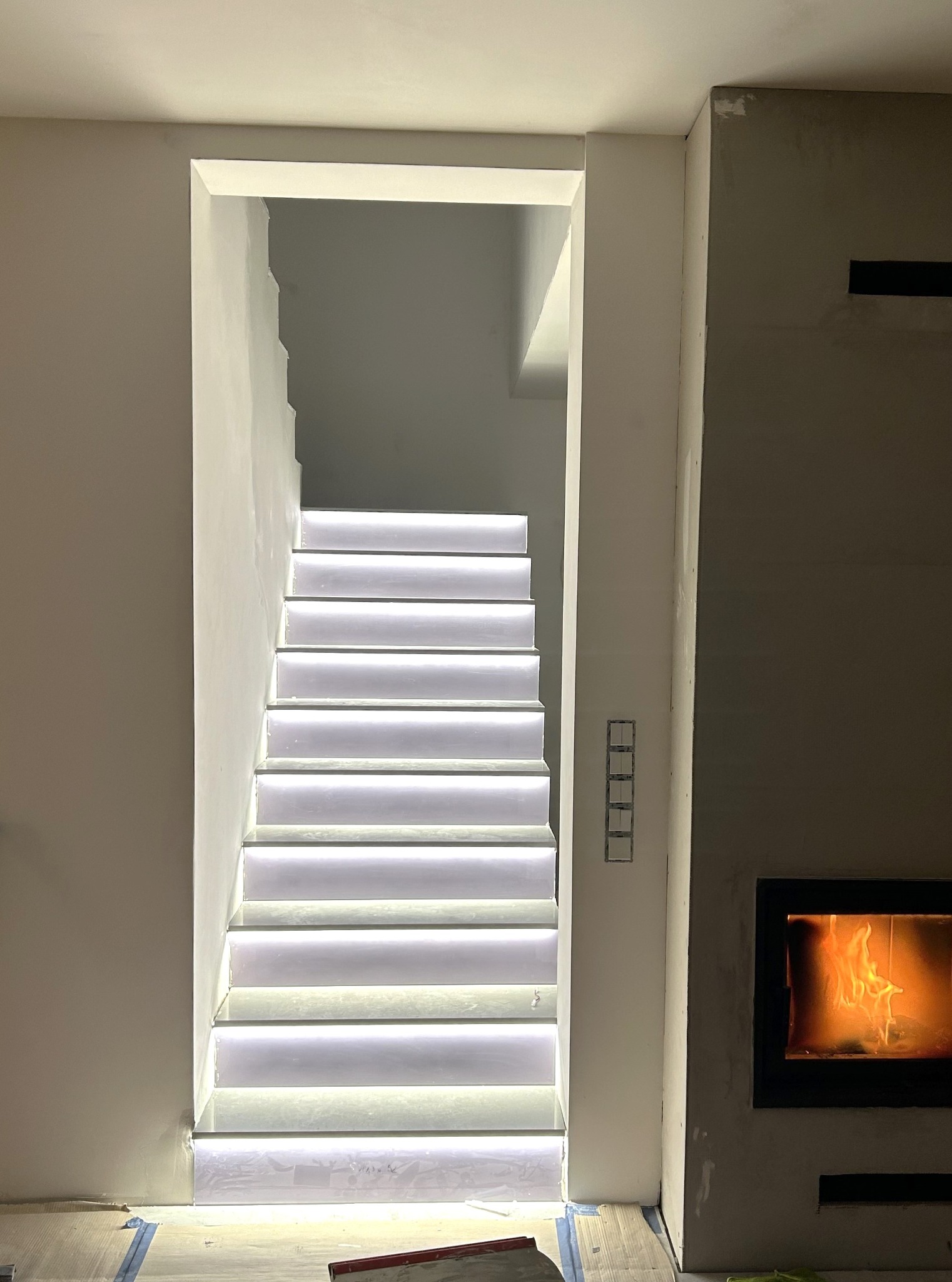 Podświetlane schody w trakcie remontu, widoczne niedokończone ściany i elementy instalacji elektrycznej. Nowoczesne oświetlenie schodów.