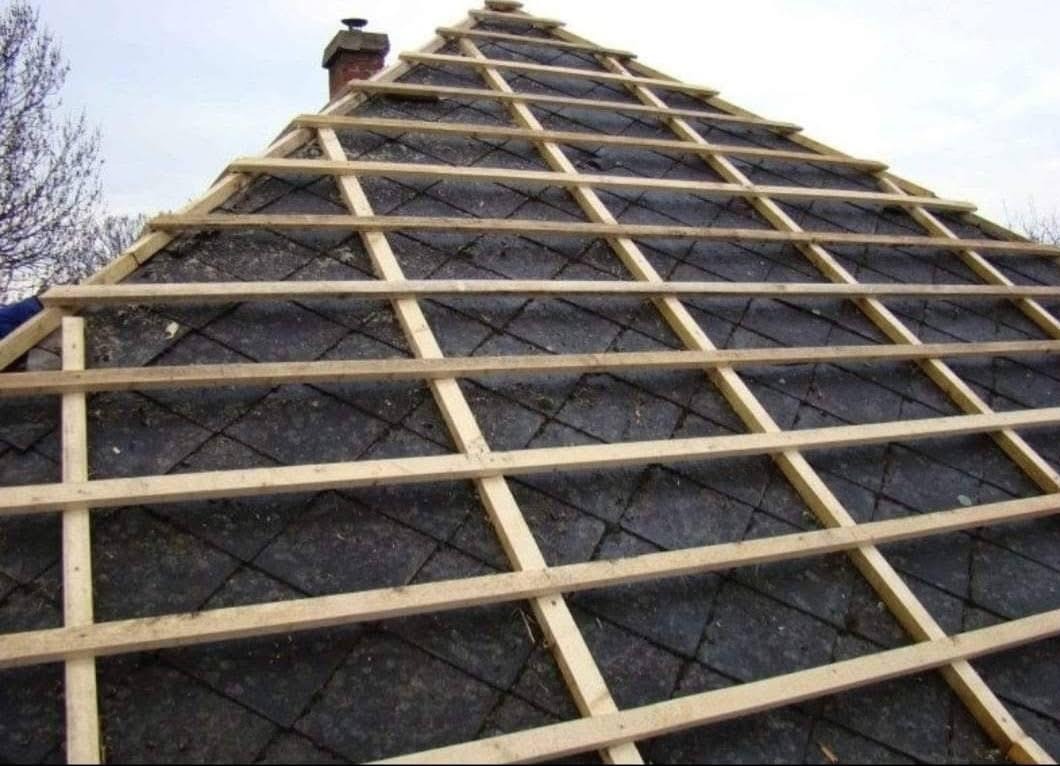 Skośny widok na dach z drewnianą konstrukcją łat, przygotowany pod nowe pokrycie, z kominem w tle i fragmentem drzewa po lewej stronie.