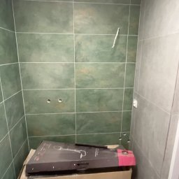 Dawid Kos - Przygotowanie do montażu armatury w łazience w Bogorii. Widoczne zielone płytki i karton z nową baterią prysznicową.