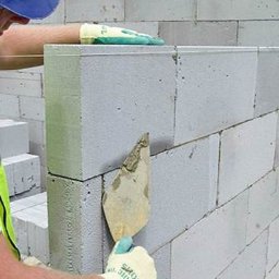 ECO PRO Ivan Pylyp - Murarz w odblaskowej kamizelce, z kielnią w dłoni, muruje ścianę z białych bloczków. Widoczna linka murarska i zapas bloczków.