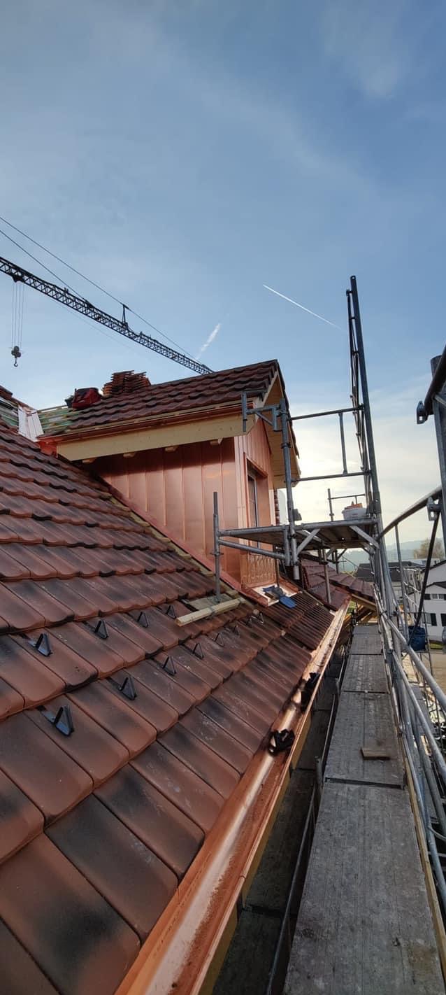 Częściowy widok dachu z nową miedzianą obróbką blacharską i rynnami, rusztowania wzdłuż krawędzi, w tle żuraw budowlany i błękitne niebo.