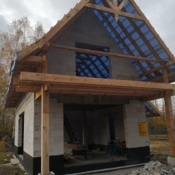 Hubert Siepiatowski - Surowy stan budynku z drewnianą więźbą dachową pokrytą niebieską folią. Widoczne bloczki betonowe i drewniane elementy konstrukcyjne. Jesienna sceneria w tle.