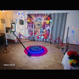 PleneroVo Events - Rozstawiona fotobudka 360 na różowym podeście, otoczona słupkami z czerwonym sznurem. W tle dekoracja 'Disco Party' z balonami i światłami dyskotekowymi.