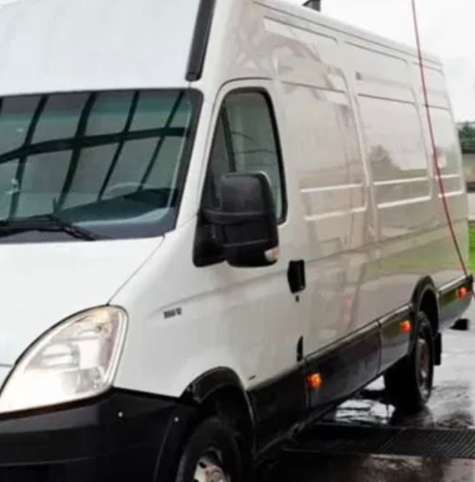 Biały bus dostawczy marki Iveco, widoczny z przodu pod kątem, po umyciu na myjni. Widoczne krople wody na karoserii i mokra nawierzchnia.