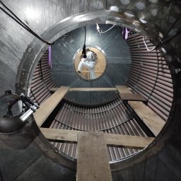 Rope - Tech Piotr Lankiewicz - Wnętrze kotła przemysłowego z pracownikiem w kombinezonie ochronnym, widoczne rury i drewniane rusztowania. Nietypowy kadr z perspektywy wnętrza urządzenia.