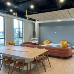 ALEKSANDER RUSAKOWICZ - Nowoczesne biuro z widocznymi instalacjami pod sufitem, oświetleniem punktowym i wiszącymi lampami. Przestrzeń relaksu z sofą i pufami, oraz stół konferencyjny z krzesłami.