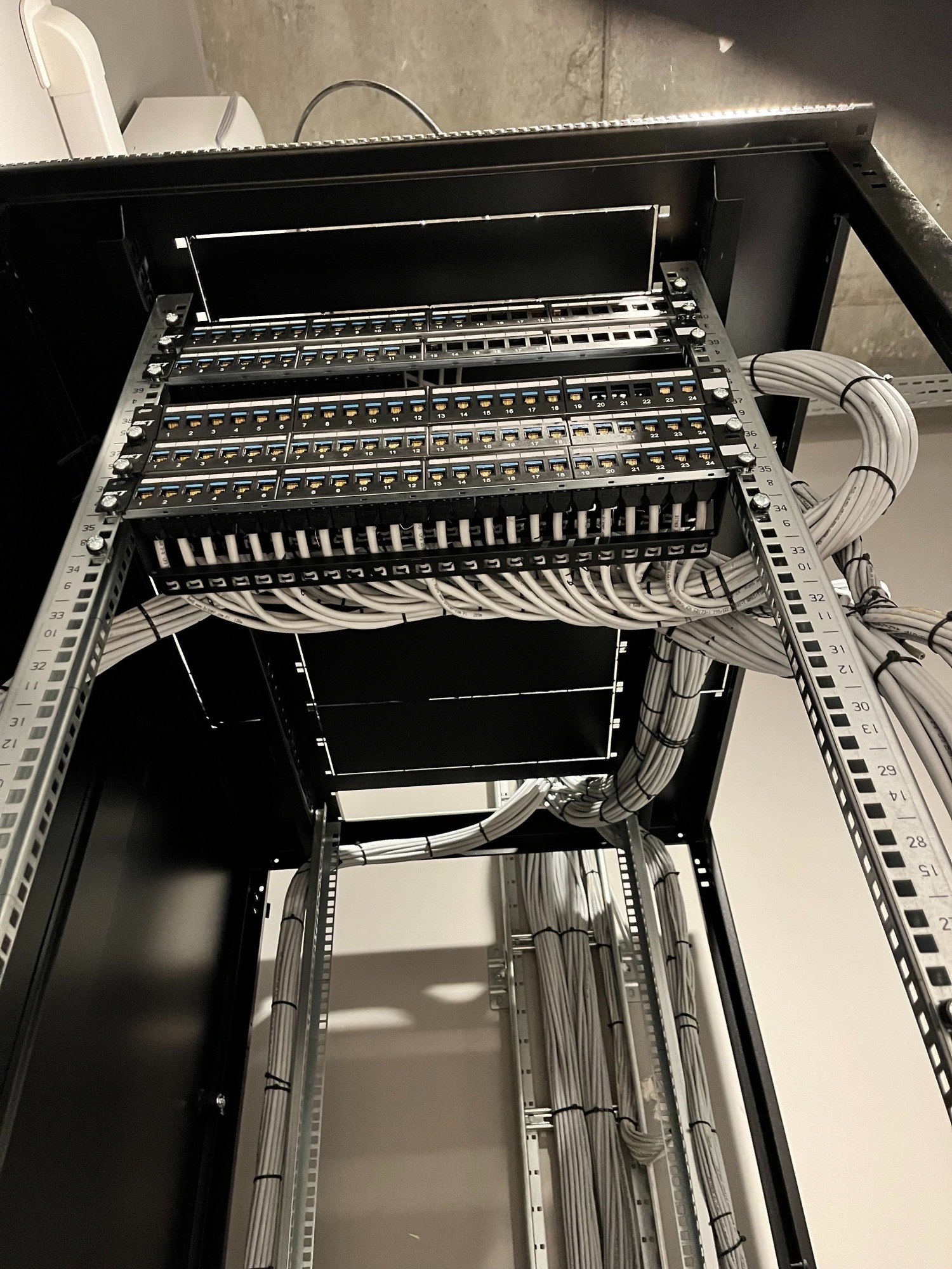 Panel krosowniczy z uporządkowanymi kablami w szafie rack, widok z dołu, oświetlenie LED, etykiety na portach, szare kable spięte opaskami.