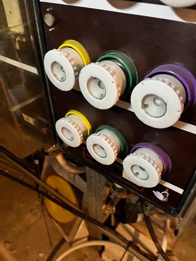 Rozdzielnica elektryczna z bezpiecznikami topikowymi oznaczonymi kolorami: żółtym, zielonym i fioletowym. Widoczne okablowanie i elementy konstrukcyjne.