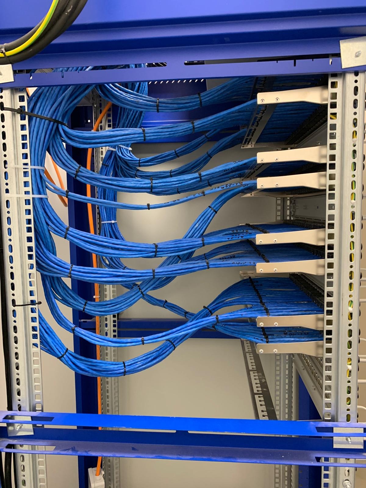 Uporządkowane, niebieskie kable sieciowe w szafie rack, spięte czarnymi opaskami. Widoczne metalowe elementy konstrukcyjne i panele krosownicze. Estetyczne prowadzenie przewodów.