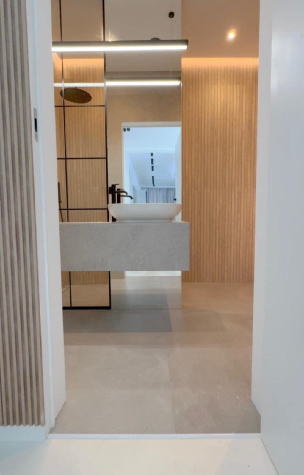 Nowoczesna łazienka z umywalką nablatową, drewnianą ścianą i kabiną prysznicową typu walk-in, widziana z perspektywy wejścia. Minimalistyczny design.