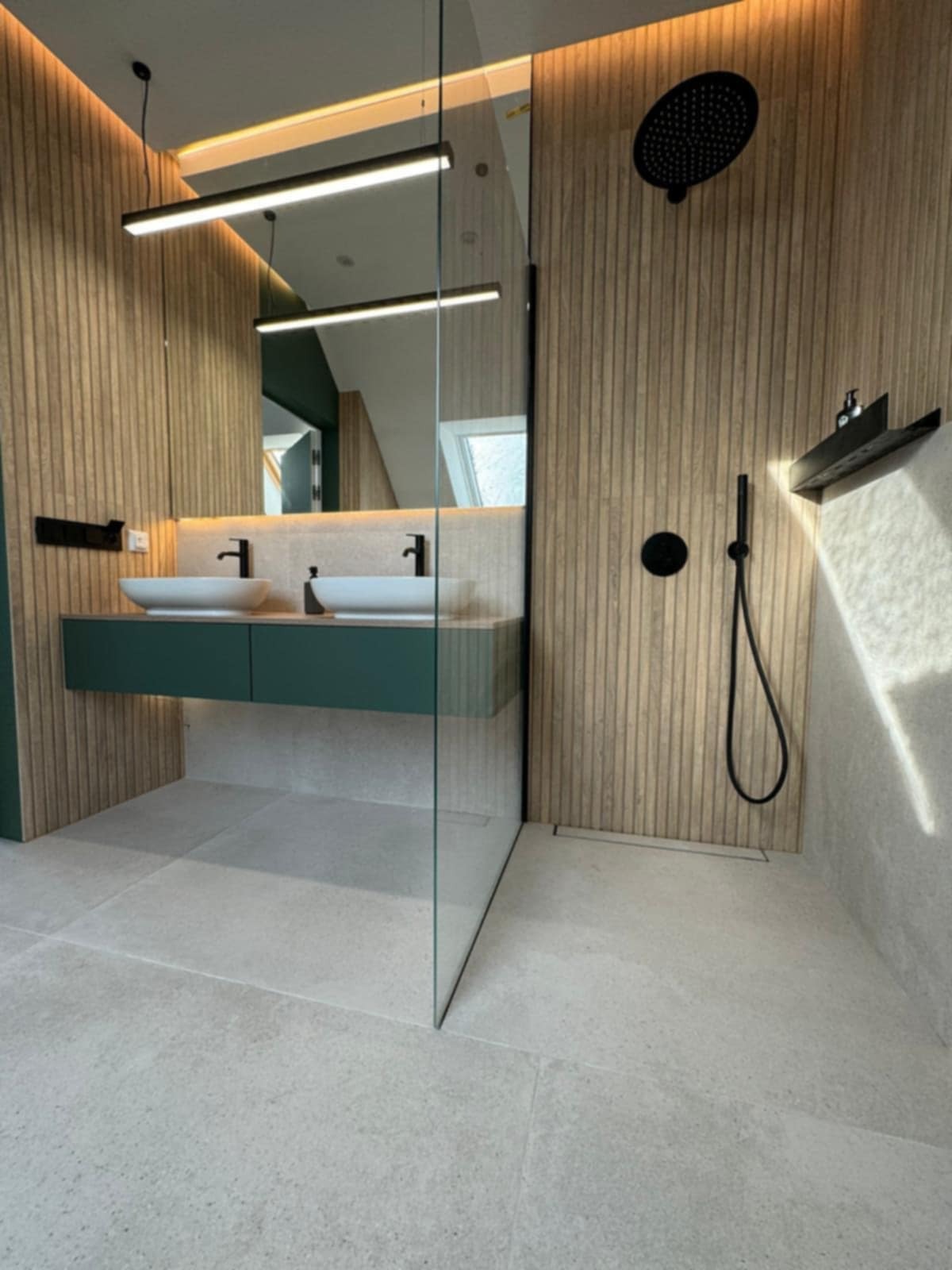 Nowoczesna łazienka z drewnianą okładziną, zieloną szafką pod umywalką i czarną armaturą. Kabina prysznicowa ze szkła.