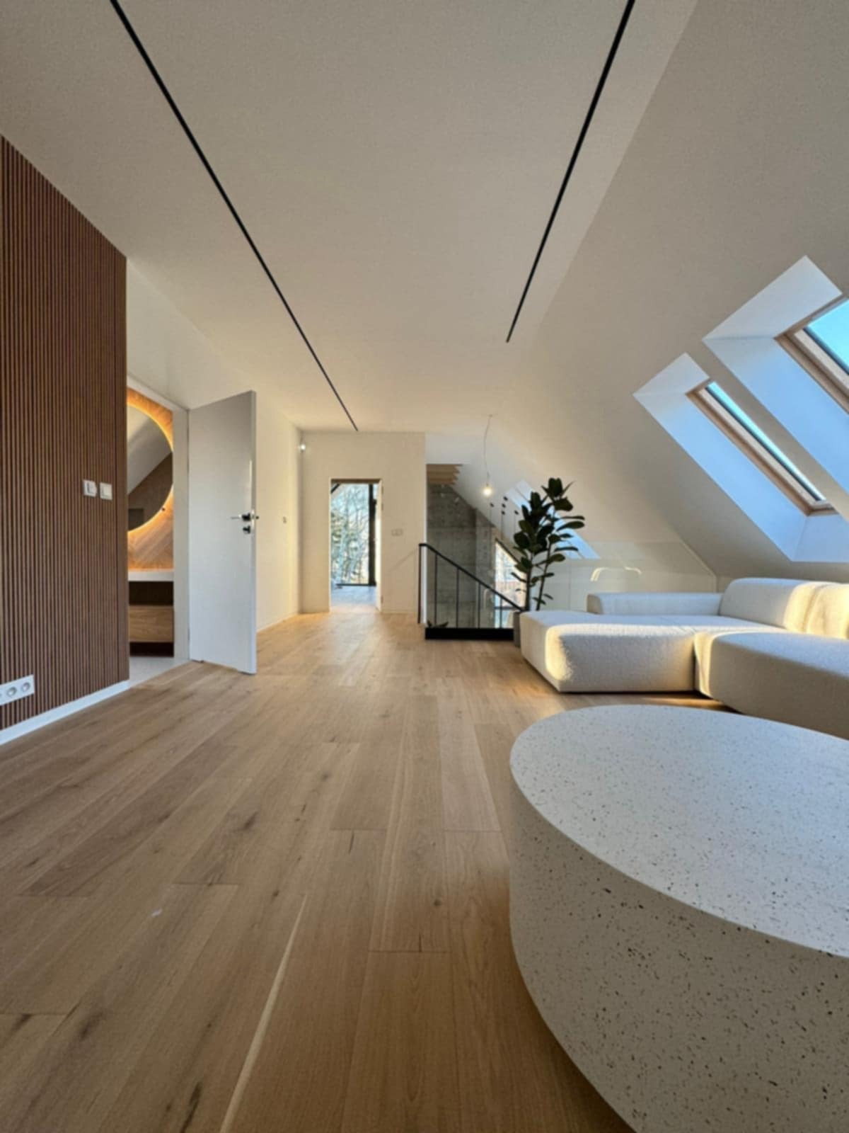 Jasne drewniane podłogi w przestronnym, nowoczesnym wnętrzu z oknami dachowymi i minimalistycznym wystrojem. Widoczny fragment sofy i stolika kawowego.
