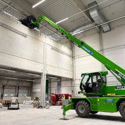 ICOOTECH SPÓŁKA Z OGRANICZONĄ ODPOWIEDZIALNOŚCIĄ - Montaż przemysłowej klimatyzacji w hali magazynowej za pomocą podnośnika teleskopowego. Widoczne elementy instalacji wentylacyjnej pod sufitem.