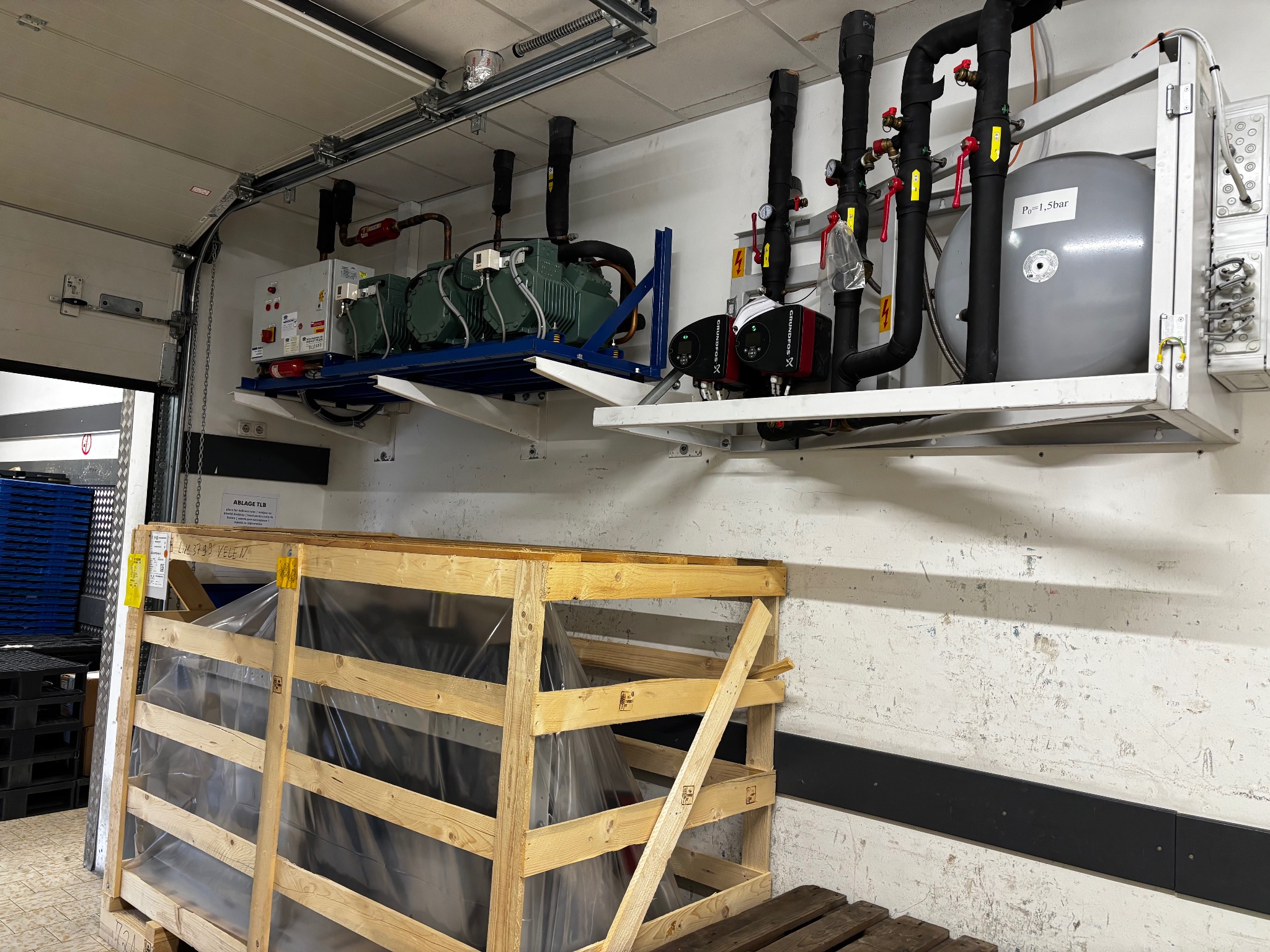 Kompleksowa instalacja chłodnicza z zielonymi sprężarkami i zbiornikiem ciśnieniowym, zamontowana w hali, widoczna skrzynia transportowa.