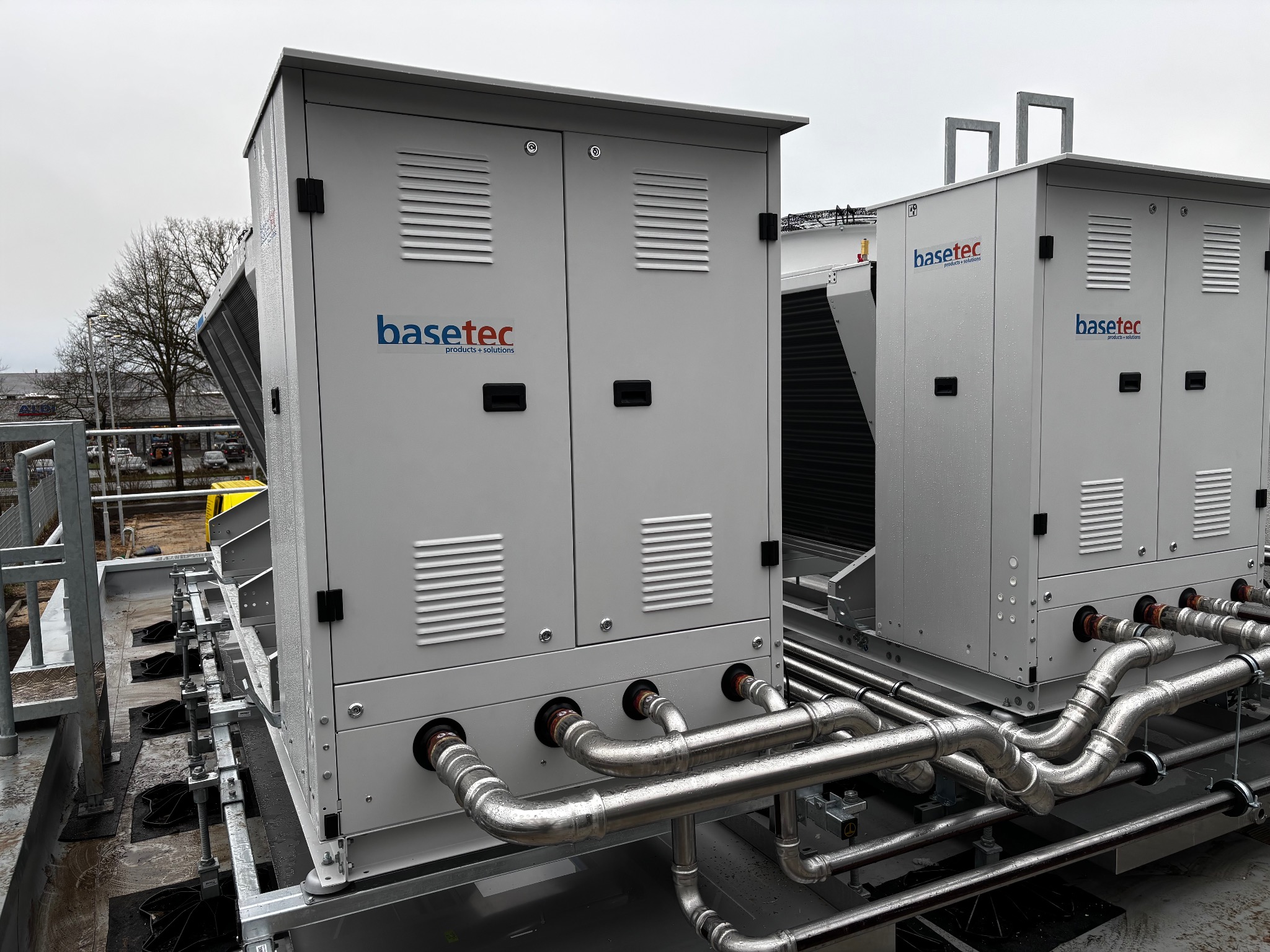 Dwa moduły klimatyzacji przemysłowej Basetec na dachu, z widocznymi rurami i kratkami wentylacyjnymi. Szary, pochmurny dzień.