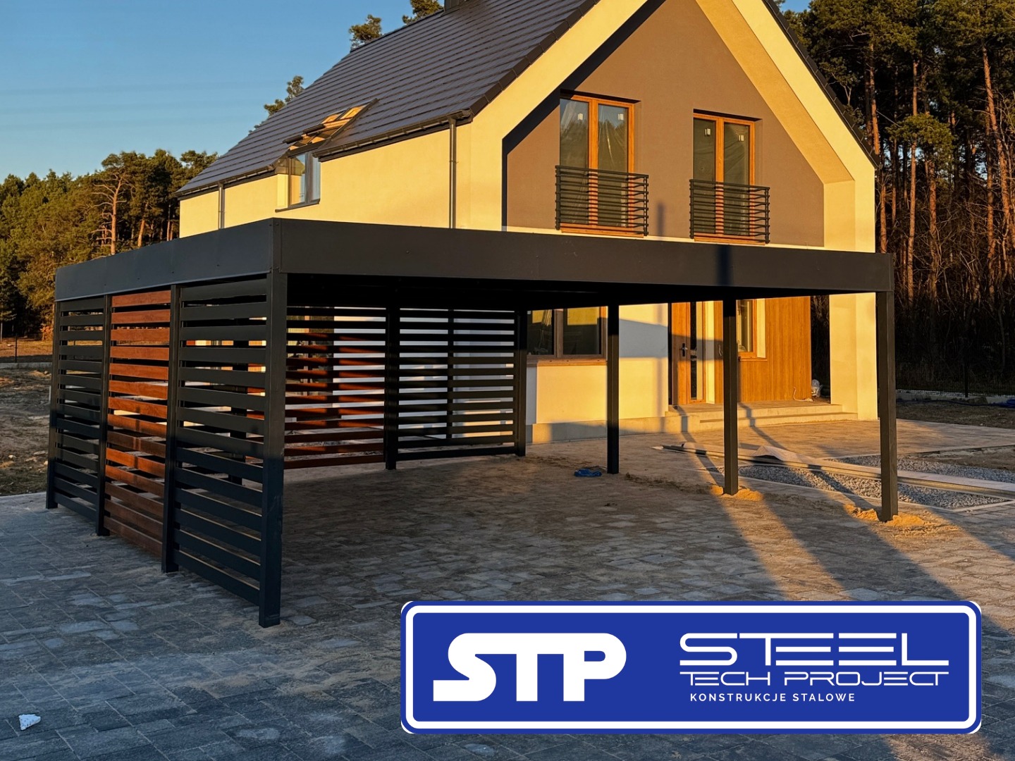 Nowoczesna, czarno-drewniana konstrukcja zadaszenia tarasu przy domu jednorodzinnym, z widocznym fragmentem elewacji i kostką brukową.