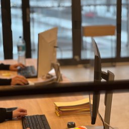 CONTA NOVA SPÓŁKA Z OGRANICZONĄ ODPOWIEDZIALNOŚCIĄ - Biuro z pracownikami przy komputerach, stos dokumentów, notatki samoprzylepne. Praca w skupieniu, jasne wnętrze z widokiem na zewnątrz.