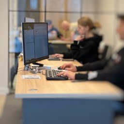 CONTA NOVA SPÓŁKA Z OGRANICZONĄ ODPOWIEDZIALNOŚCIĄ - Praca biurowa: osoba przy komputerze, dłonie na klawiaturze, monitor z danymi, w tle inni pracownicy. Jasne biuro, nowoczesny design.