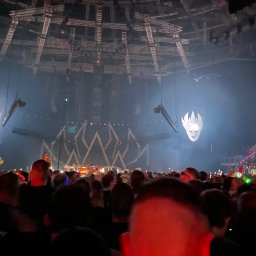 ATŁABUD - Widok na scenę z tłumu podczas koncertu. W tle dekoracje sceniczne i oświetlenie. Widać publiczność z podniesionymi rękami i telefonami.