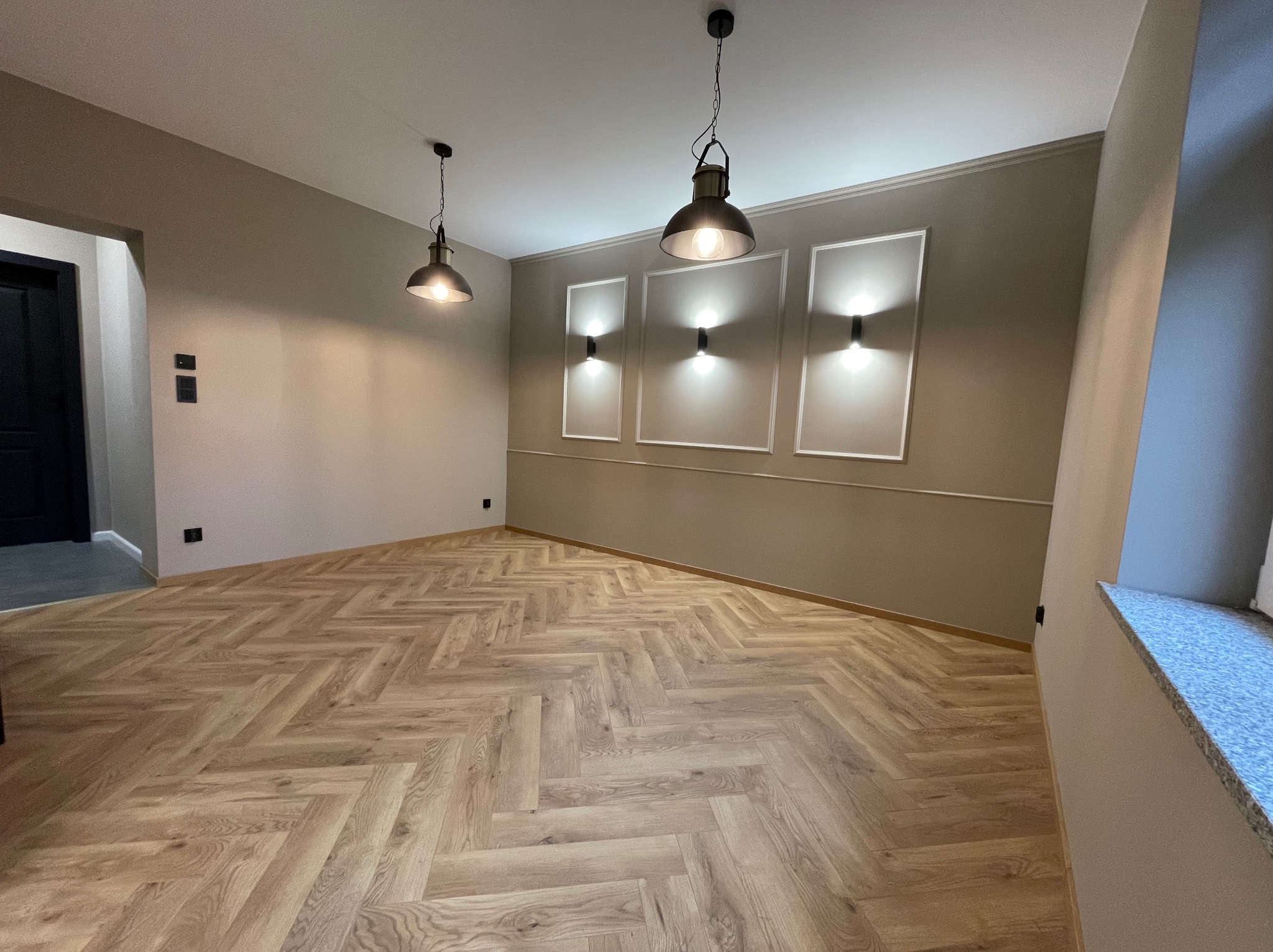 Jasne panele ułożone w jodełkę, szare ściany z dekoracyjnymi listwami i lampy w stylu industrialnym w Obornikach Śląskich. Nowoczesne wykończenie wnętrza.