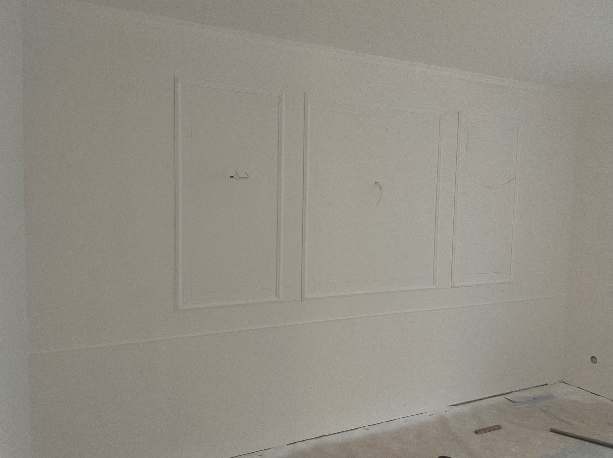 Białe, świeżo pomalowane wnętrze z dekoracyjnymi panelami ściennymi i listwami przypodłogowymi. Widoczne ślady po pracach wykończeniowych na podłodze.