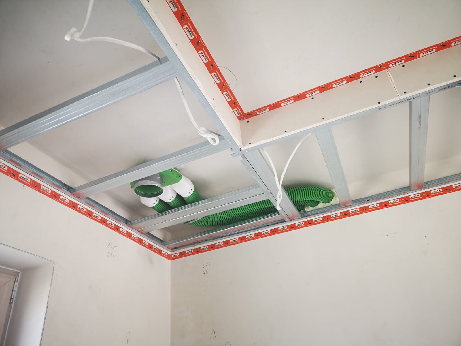 Sufit podwieszany z płyt kartonowo-gipsowych w trakcie montażu, widoczne profile metalowe, taśma uszczelniająca i instalacja wentylacyjna w kolorze zielonym.