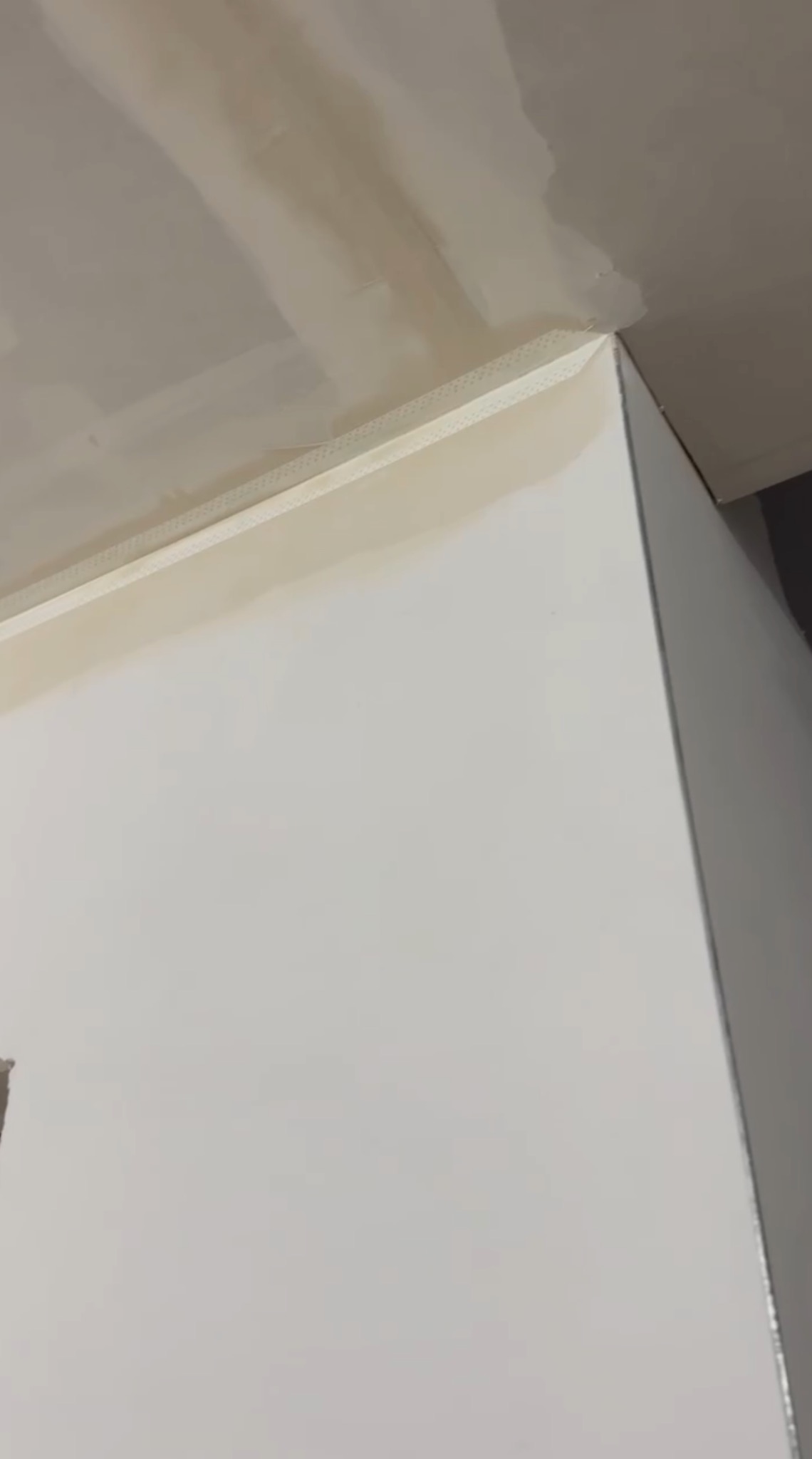 Wnętrze po szpachlowaniu: gładka, biała ściana z widoczną taśmą wzmacniającą na styku ze sufitem. Przygotowanie do malowania.