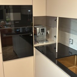 Artwood - Jasna zabudowa kuchenna z czarnym blatem, wnęką na ekspres do kawy i piekarnikiem Samsung. Parkiet ułożony w jodełkę na podłodze.