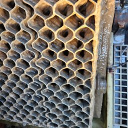 BIO-SET SPÓŁKA Z OGRANICZONĄ ODPOWIEDZIALNOŚCIĄ - Filtr o strukturze plastra miodu, pokryty osadem, prawdopodobnie element oczyszczalni ścieków. Widoczne zabrudzenia i detale konstrukcji.