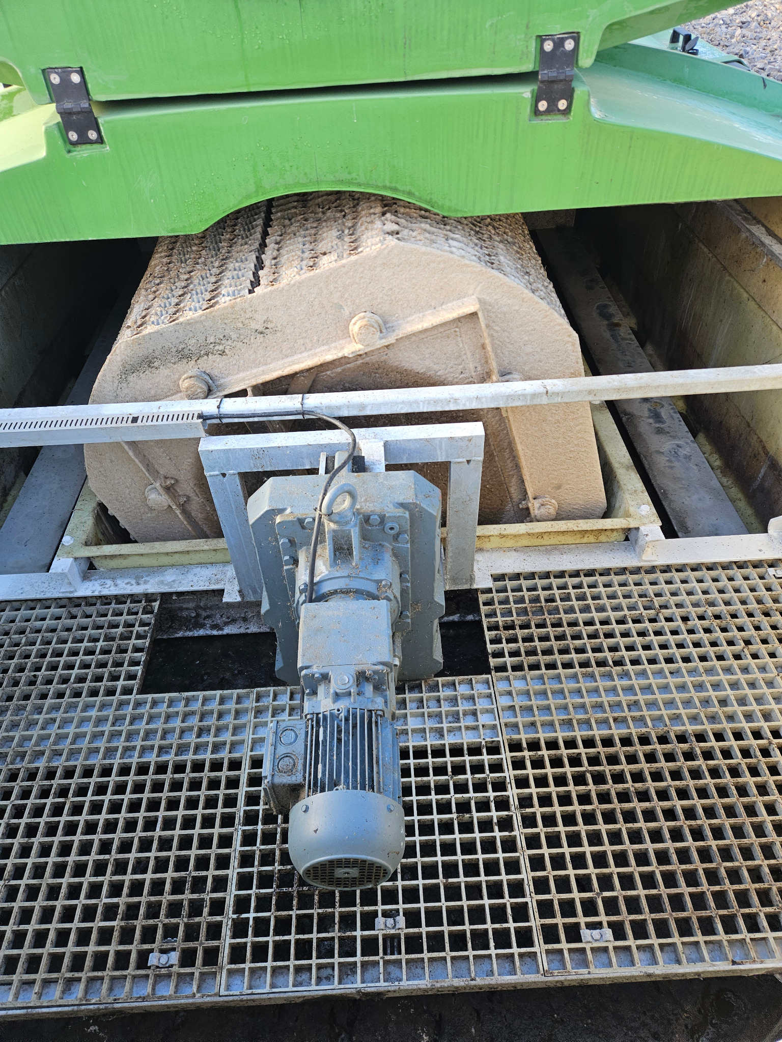 Fragment mechanizmu oczyszczalni ścieków z silnikiem w Wojnowie, widoczny przez kratę. Elementy konstrukcyjne w odcieniach szarości i zieleni, z osadami.