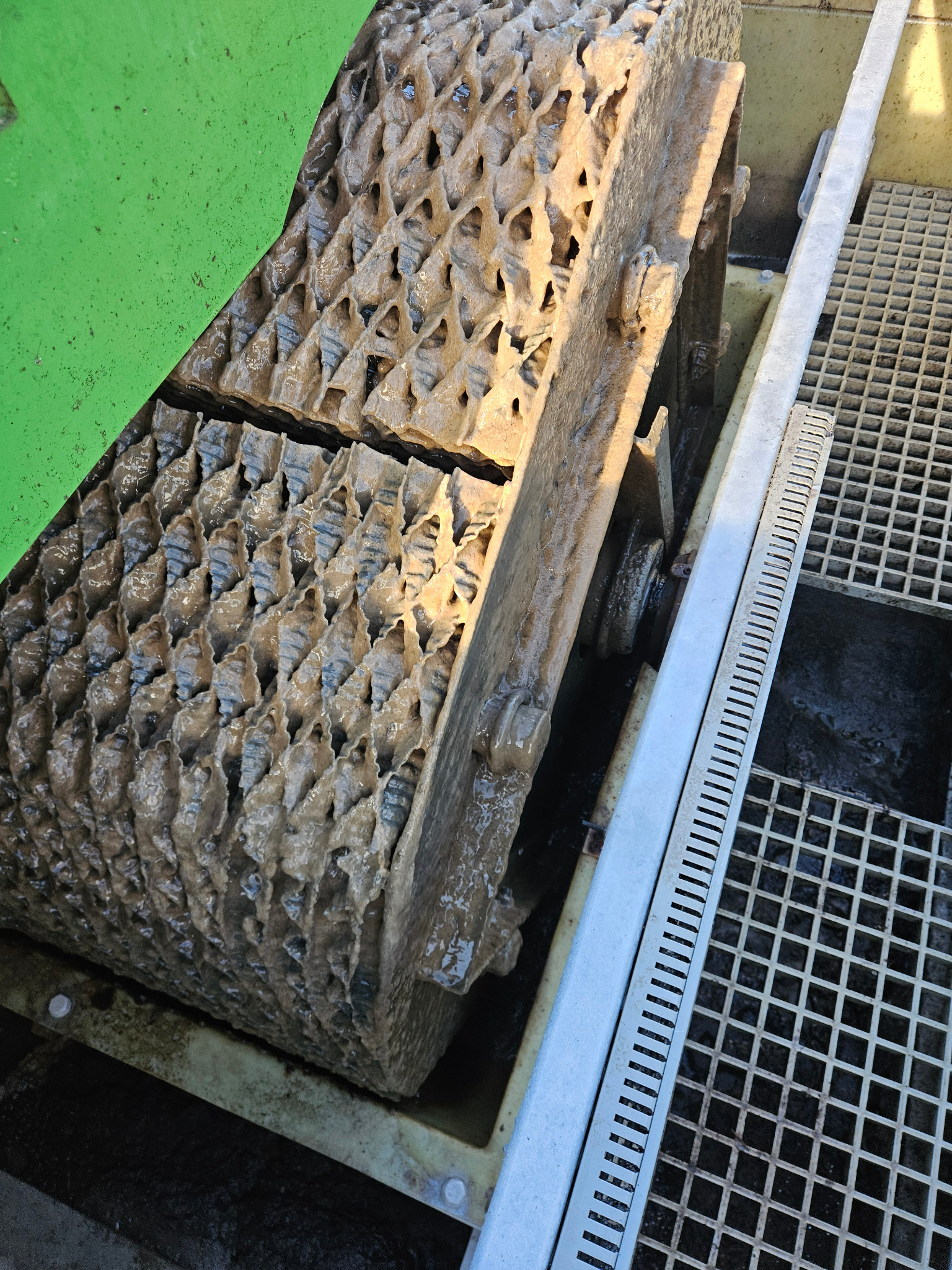 Fragment zanieczyszczonego, obrotowego złoża biologicznego w oczyszczalni ścieków. Widoczne elementy konstrukcyjne i kraty. Ujęcie z góry, ostre światło.