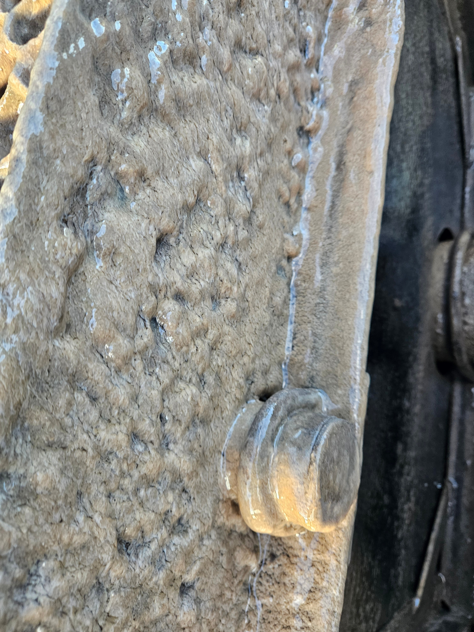 Szczegółowe ujęcie fragmentu betonowego szamba z widoczną strukturą i śladami wilgoci, uchwycone pod nietypowym kątem, podkreślające surowość materiału.