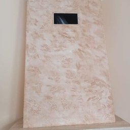 SEB-BUD Sebastian Żebczyński - Otynkowana obudowa kominka z otworem wentylacyjnym, dekoracyjna faktura w odcieniach beżu i brązu, widok z dołu, fragment marmurowego blatu kominka.