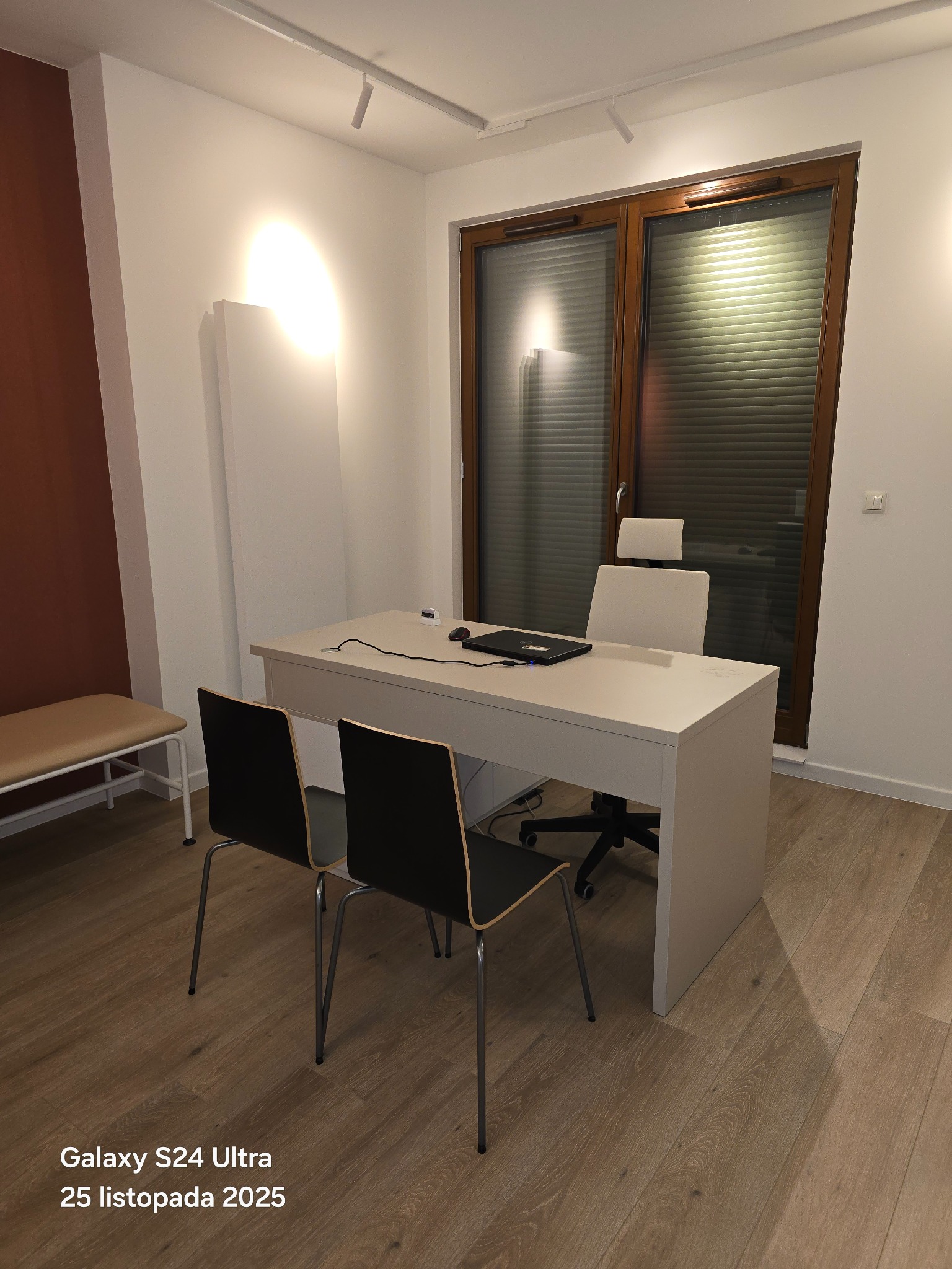 Jasne biuro po remoncie: biurko z laptopem, krzesła, drewniana podłoga, okno z żaluzjami. Minimalistyczny design, ciepłe oświetlenie.