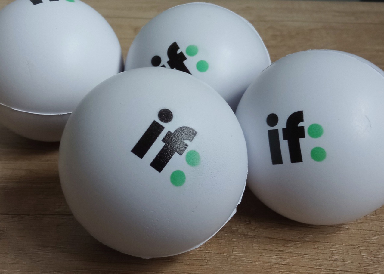 Cztery białe piłeczki antystresowe z czarno-zielonym logo 'if:' na drewnianym tle, ukazujące branding firmy w formie gadżetów reklamowych.