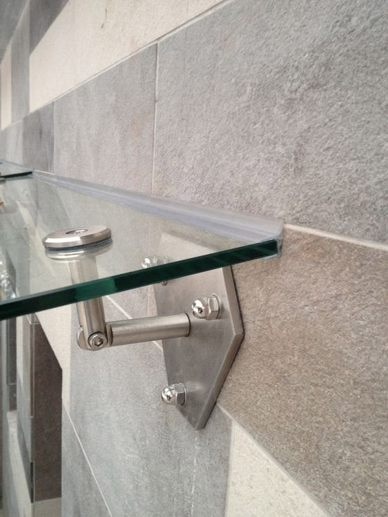 Szklana balustrada mocowana do ściany z płytek. Widoczne metalowe elementy mocujące i krawędź szkła z uszczelką. Ujęcie z bliska, skupione na detalu.