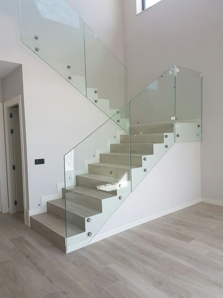 Nowoczesne schody z jasnymi stopniami i szklaną balustradą mocowaną punktowo, widoczne w przestronnym wnętrzu w Michałowicach. Minimalistyczny design.