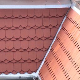 Hubert Siepak - Czerwona dachówka karpiówka na dachu z nową, srebrną rynną. Widok z góry, ukazujący detale pokrycia i orynnowania.