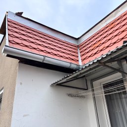 Hubert Siepak - Czerwona dachówka karpiówka na dachu budynku z zamontowaną rynną. Widoczna elewacja budynku z oknem i suszarką na pranie.