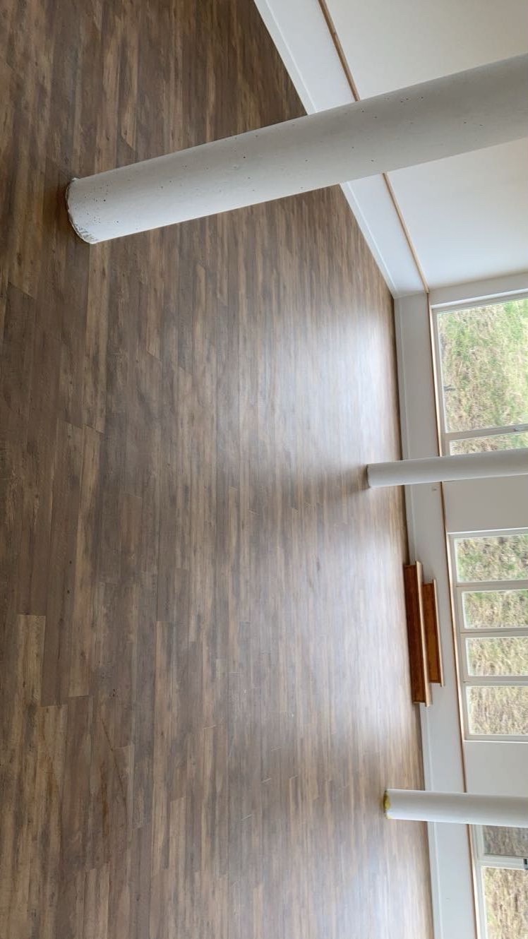 Ułożone panele podłogowe w jasnym wnętrzu z kolumnami i oknami. Widok z góry ukazuje wzór drewna i detale wykończenia.