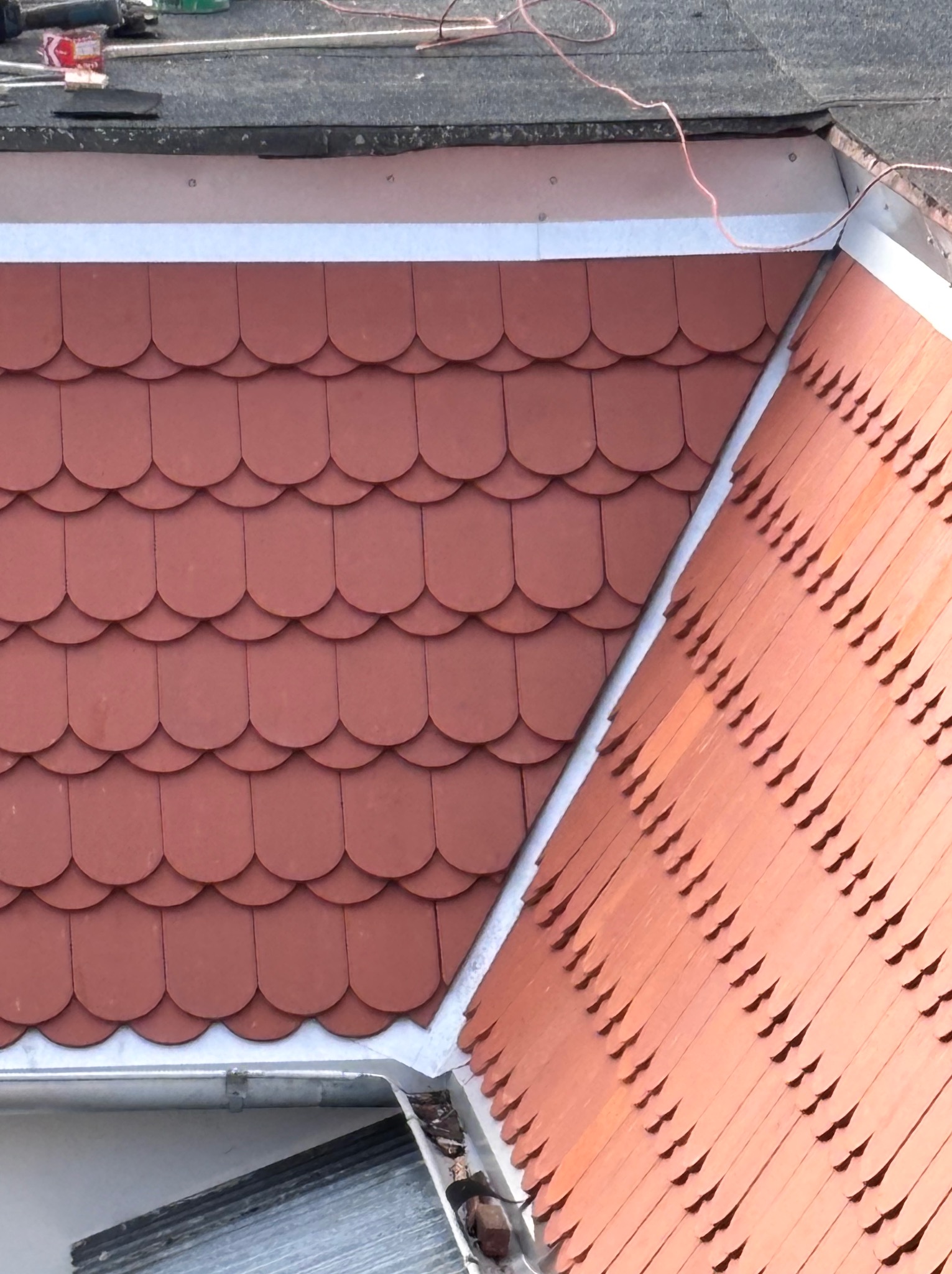 Czerwona dachówka karpiówka na dachu z nową, srebrną rynną. Widok z góry, ukazujący detale pokrycia i orynnowania.