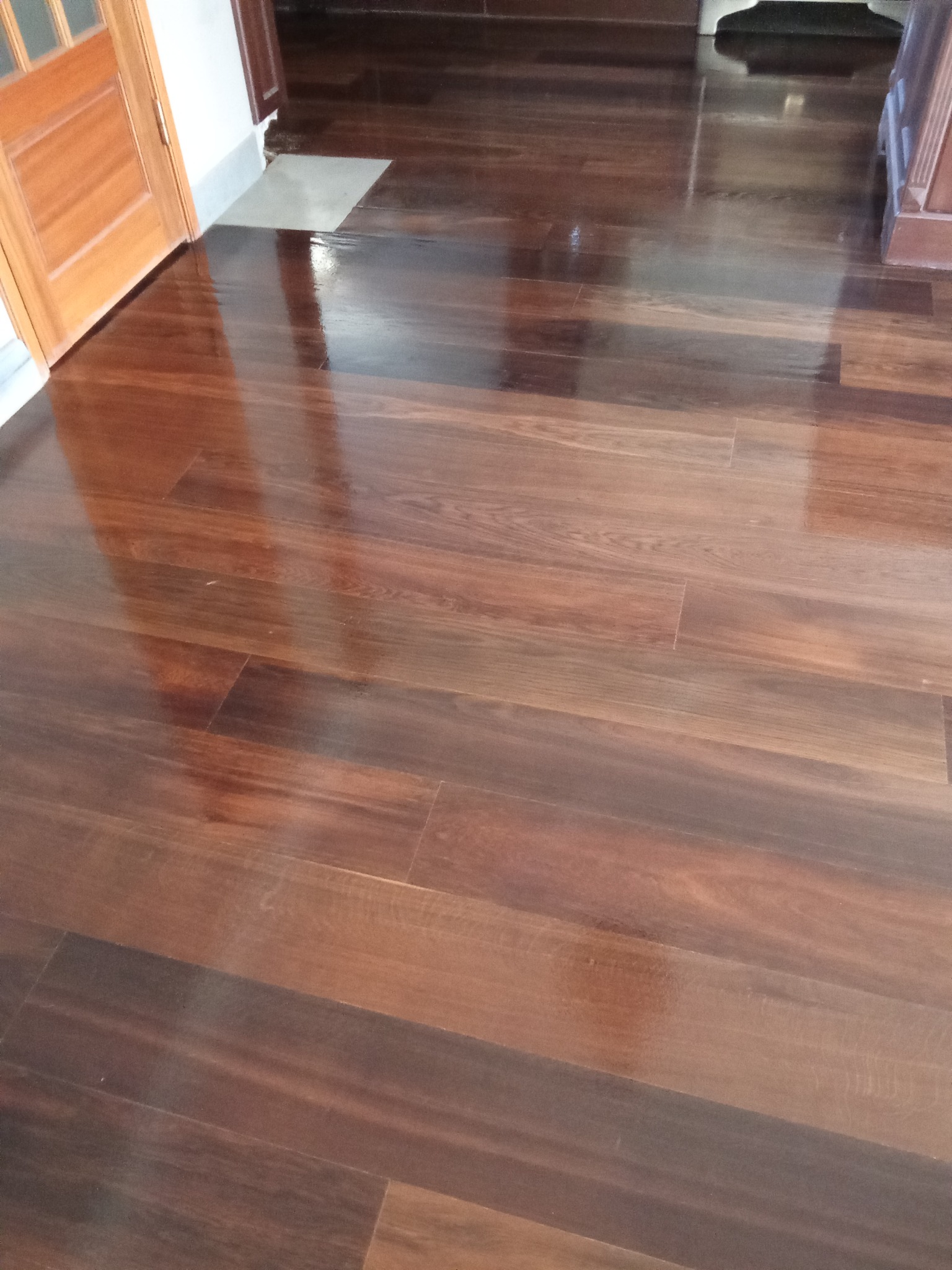 Błyszcząca, ciemna podłoga z parkietu ułożonego w regularny wzór, odbijająca światło. Widoczny fragment drzwi i listwy przypodłogowej.