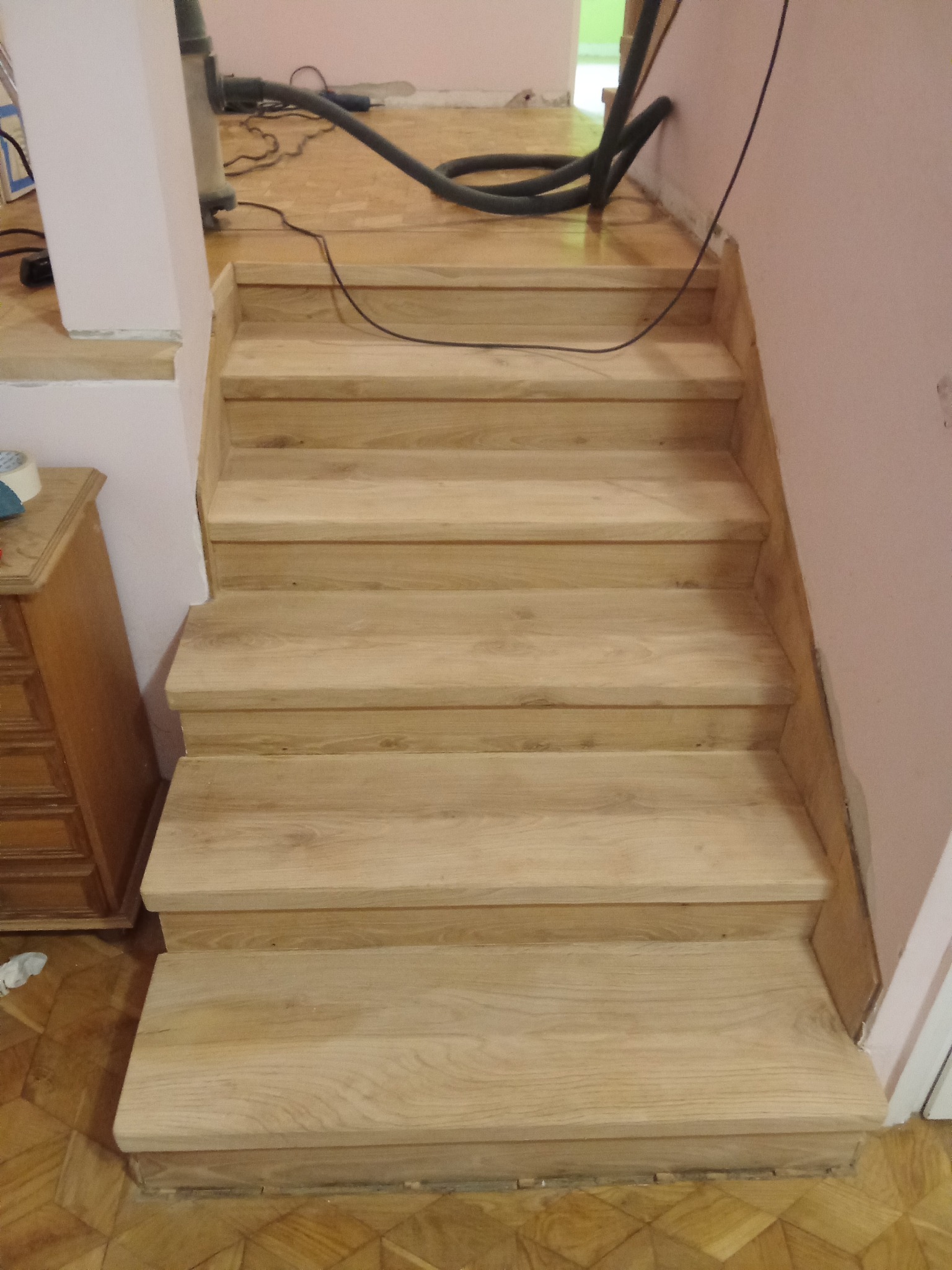 Jasne, drewniane schody po renowacji, widoczne ślady prac wykończeniowych i odkurzacz. Świeżo wykończone stopnie schodów z naturalnego drewna.