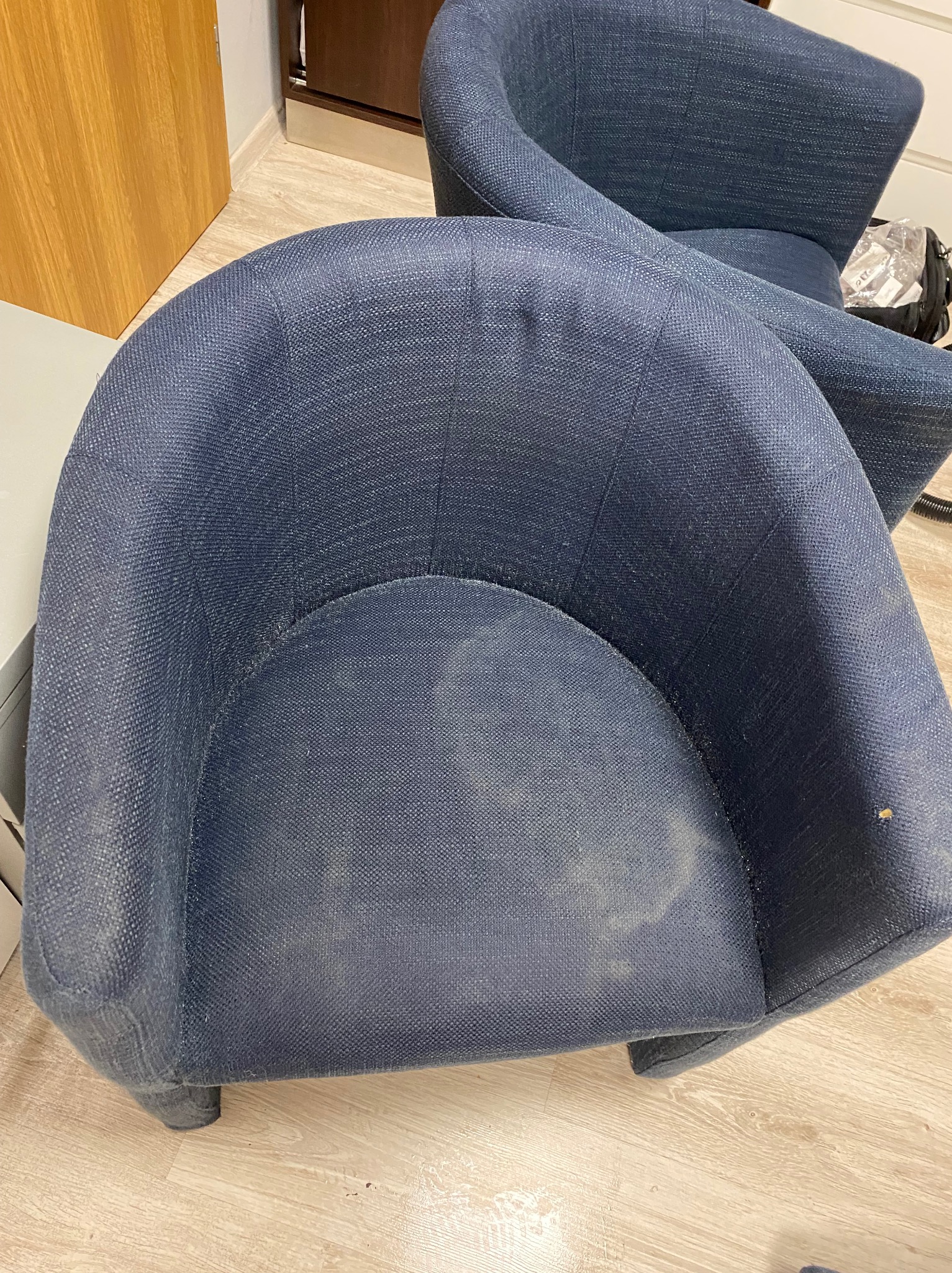 Dwa niebieskie, tapicerowane fotele w pomieszczeniu. Na siedzisku jednego z nich widoczne plamy, co sugeruje potrzebę prania tapicerki.