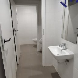 KS-BUD Serhii Koshil - Wnętrze łazienki z umywalką, lustrem i otwartymi drzwiami do toalety. Widoczne szare płytki podłogowe i białe ściany. Minimalistyczny design.