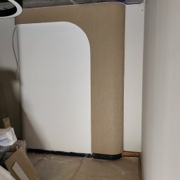 KS-BUD Serhii Koshil - Wykończone przejście w ścianie z zaokrąglonym narożnikiem, obłożone tapetą w odcieniach beżu. Widoczne materiały budowlane i surowy sufit.