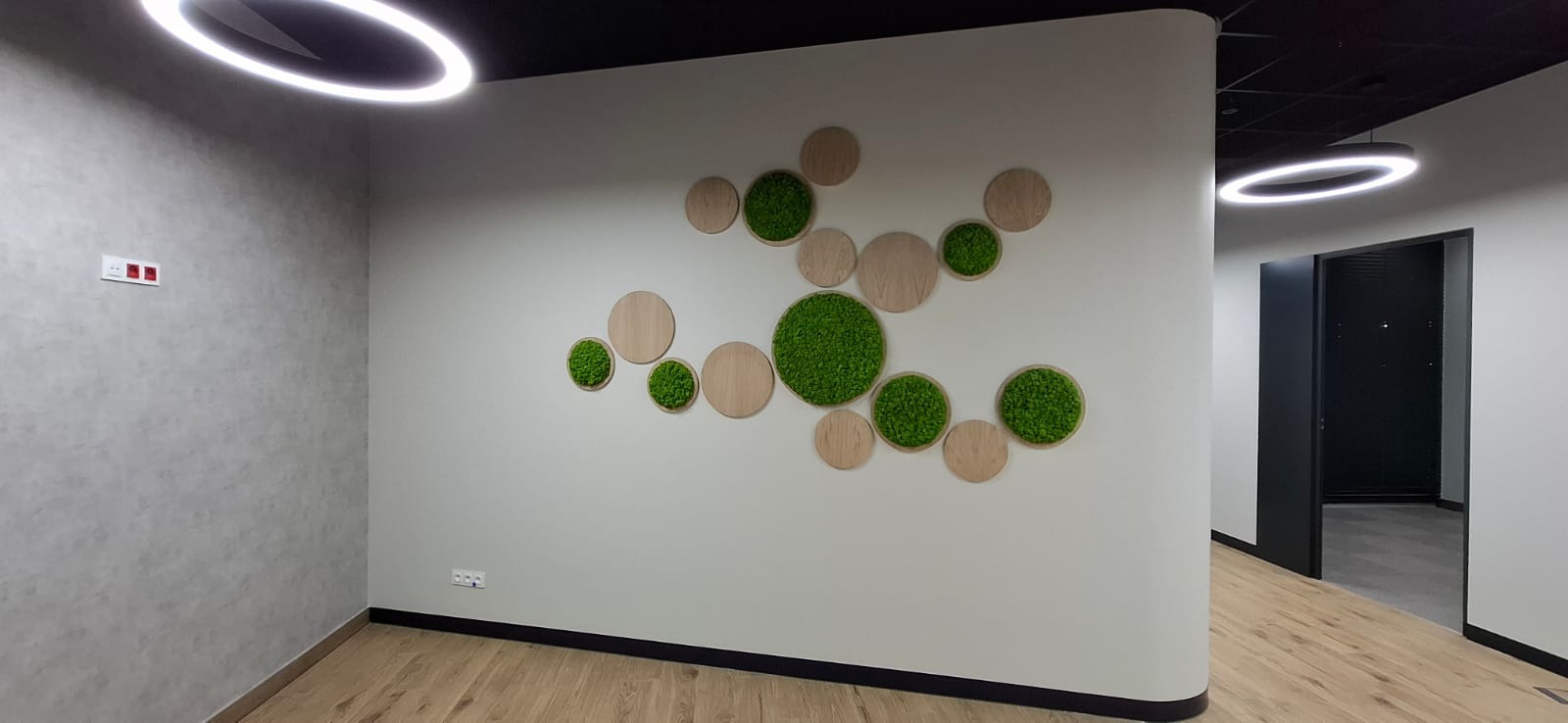 Nowoczesne wykończenie biura: ściana z dekoracją z mchu w drewnianych okręgach, parkiet, oświetlenie LED. Minimalistyczny design, jasne kolory, czarne akcenty.
