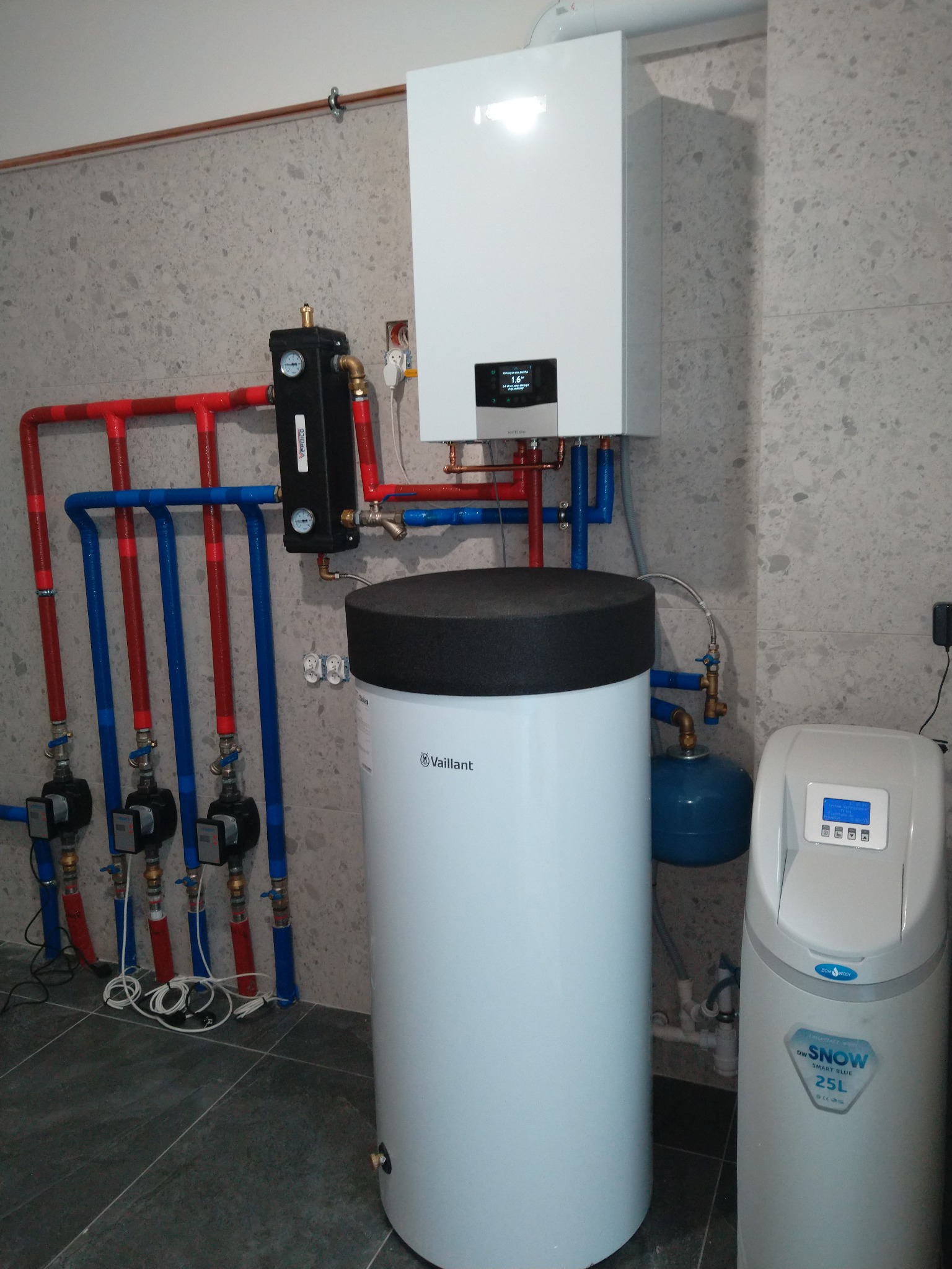 Nowoczesna kotłownia z piecem gazowym, zasobnikiem CWU Vaillant i zmiękczaczem wody DW Snow. Instalacja z rur miedzianych w kolorach czerwonym i niebieskim.